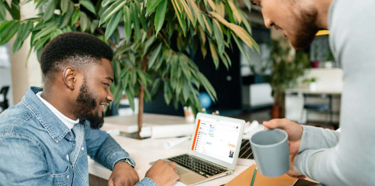 Deux personnes regardent un ordinateur affichant l'interface de Linphone. La personne au premier plan sourit, tandis que l'autre, en arrière-plan, boit une tasse de thé.